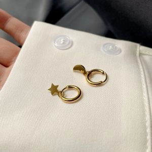 Détail de boucles d'oreilles asymétriques étoile et lune dorées sur une chemise