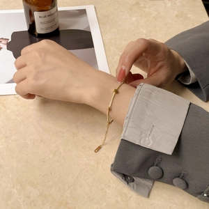 Detailed view of an 18K gold bracelet featuring delicate beads and square charms on the wrist