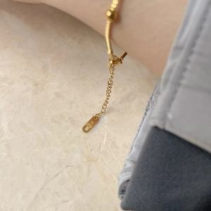 Close-up of gold chain bracelet with beads and detailed K18 hallmark on oval tag
