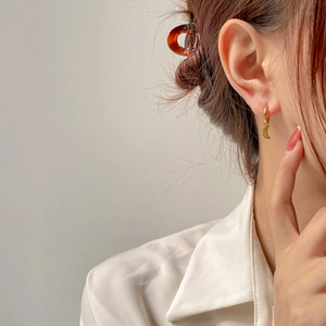 Détail de boucles d'oreilles asymétriques dorées avec charmes étoile et lune sur modèle