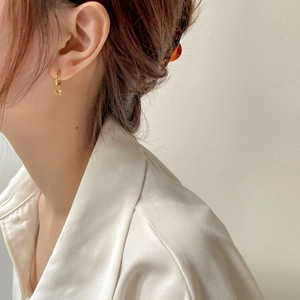 Détail d'une boucle d'oreille étoile dorée minimaliste portée avec un chemisier en soie