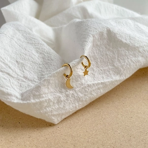 Détail de créoles dorées asymétriques avec pendentifs étoile et lune sur tissu