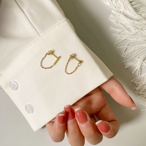 Close-up of gold chain tassel earrings on white shirt sleeve with soft lighting