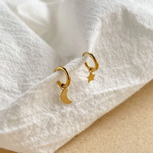 Détail de boucles d'oreilles créoles asymétriques étoile et lune dorées sur tissu blanc