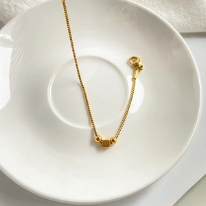 Detail of a gold box chain bracelet with polished round and square beads and lobster clasp