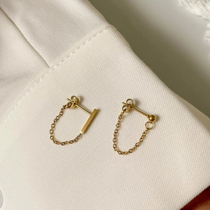 Elegant gold tassel chain earrings on white fabric background, minimalist fashion jewelry