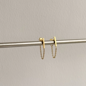 Detailed view of elegant gold chain tassel earrings on a metallic display bar