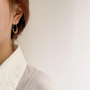 Close-up of elegant gold U-shaped oval hoop earring worn by a model on plain background