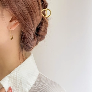 Detail of gold U-shaped earrings and twisted metal hair claw on a female model