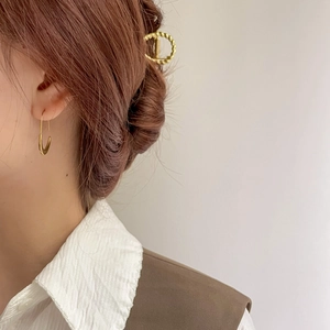 Detail of golden U-shaped earrings and textured hair clip shown on a model