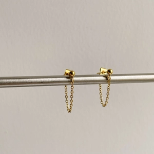 Detailed view of minimalist gold chain tassel earrings hanging on a metal bar