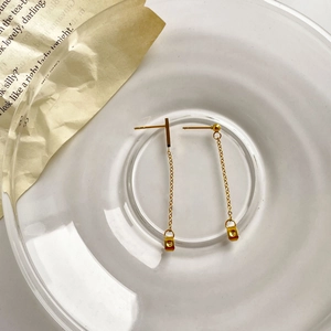 Detail of long gold tassel drop earrings with chain and square pendant on a glass tray