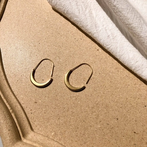 Macro detail of gold crescent earrings with a matte finish and U-shaped hanging hooks