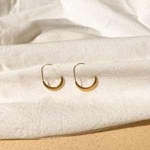 Detailed close-up of French-style gold u-shaped oval hoop earrings on white linen fabric