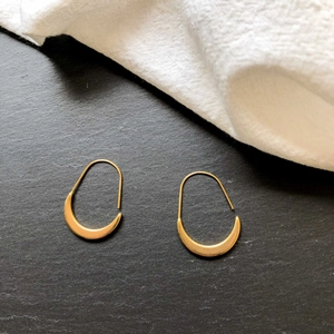 Detailed view of minimalist gold crescent hoop earrings on a textured stone surface