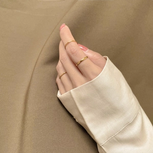 Three thin minimalist polished gold-plated stackable rings worn on a hand with nude nails