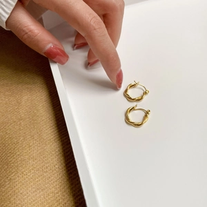 Gold twisted rope hoop earrings with S-hook closure shown on a minimalist warm background