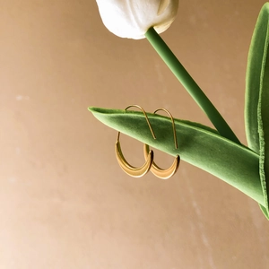 Minimalist gold crescent hoop earrings displayed on a fresh tulip leaf with matte finish