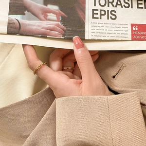 Detail of elegant gold twist and fine chain rings on model with chic beige blazer