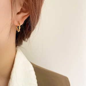 Close-up of elegant gold twisted hoop earrings worn by a model in a minimal setting