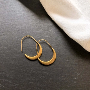 Detail of gold crescent earrings with matte brushed finish on a dark stone surface