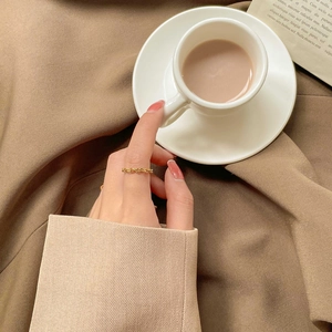 Detail of a gold braided chain ring worn on the finger with a warm aesthetic background