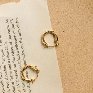 Minimalist twisted gold hoop earrings with textured metal finish on vintage background