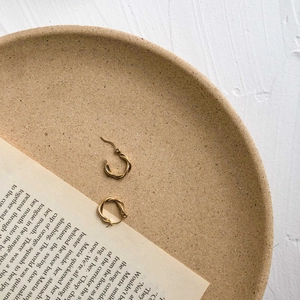 Detail shot of golden twisted hoop earrings on an open book with warm natural lighting