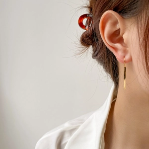 Close-up of minimalist long gold drop earrings with polished finish on a female model