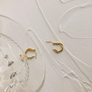 Detailed close-up of gold twisted rope hoop earrings on white stone surface