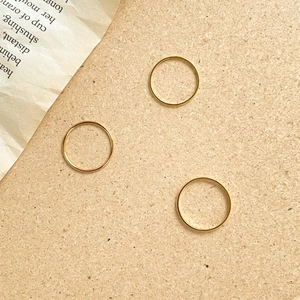 Close-up of three minimalist thin gold stackable rings arranged on a warm cork surface