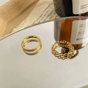 Close-up of golden braided twist and chunky chain link rings on reflective surface