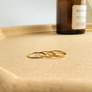Detailed view of three minimalist gold-plated stacking rings on a textured tray