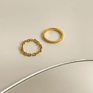 Detail of two gold chain link rings with intricate twisted rope texture on a mirror base