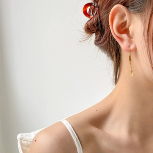 Close-up of golden minimalist twisted bar earrings worn by a model in soft light