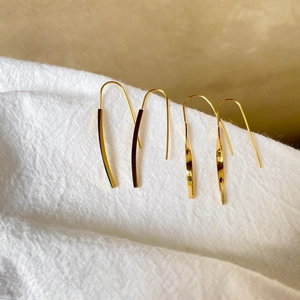 Close-up of minimalist gold twisted drop earrings on textured white fabric background