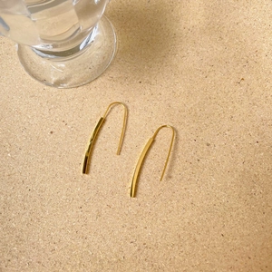 Minimalist twisted gold bar earrings with polished finish on a rustic cork texture