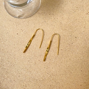 Macro shot of minimalist gold twist geometric drop earrings on a natural cork texture