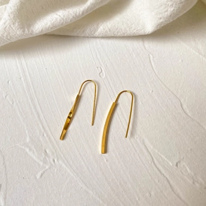 Macro shot of minimalist long bar drop earrings with gold plating on textured background