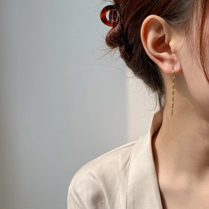 Detail of golden long tassel earrings with diamond shape chain on female model