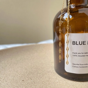 Close-up of a gold chain with sunburst textured oval links hanging on a vintage bottle