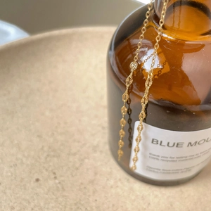 Detailed view of the delicate golden disc chain draped over a decorative glass bottle