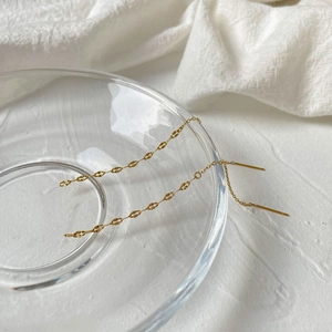 Detail of elegant gold drop chain earrings featuring textured oval links on glass
