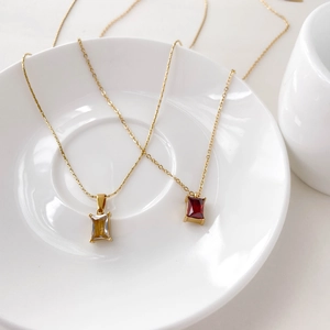 Macro shot of rectangular zircon pendant necklaces with red and clear gems on ceramic