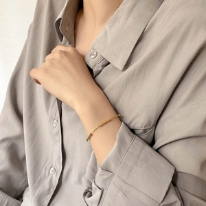 Minimalist gold bar chain bracelet shown on woman wrist over grey linen clothing