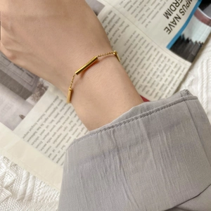 Detailed view of a minimalist gold bar chain bracelet worn on a woman's wrist