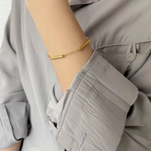 Detail of minimalist gold chain bracelet with polished bar on a linen shirt sleeve