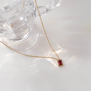 Macro shot of rectangular red gemstone pendant on a gold necklace with natural light shadows