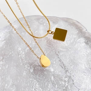 Détails de colliers dorés avec pendentifs carrés et gouttes sur surface en verre