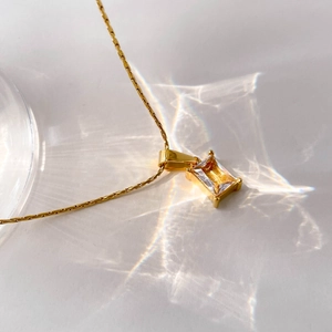 Macro detail of a gold chain necklace featuring a square-cut clear crystal pendant